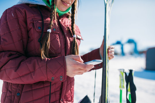 Female skier holds skis and mobile phone in hands