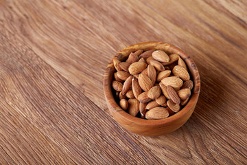 Bowl of almonds on wooden background, top view, close-up, selective focus.