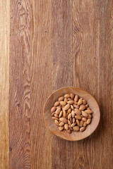 Bowl of almonds on wooden background, top view, close-up, selective focus.