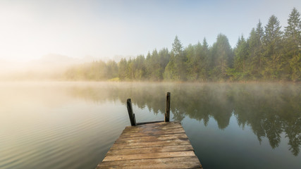 Steg am See in den Alpen im Sonnenaufgang mit Nebel