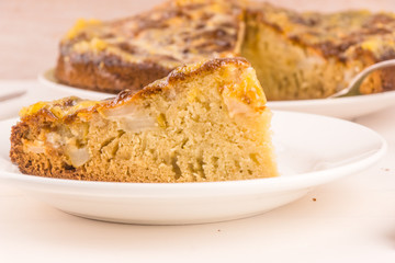 A piece of French apple cake on a plate on a light wooden background