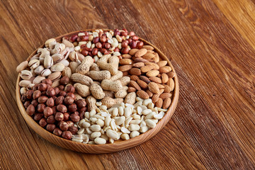 Mixed nuts arrenged on wooden tray over rustic background, close-up, selective focus.