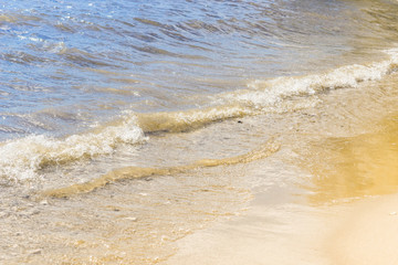 Coast of the sea on a sunny day with blue waves and yellow sand - the concept of relaxation