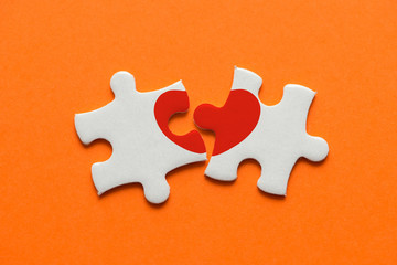 closeup of two pieces of a puzzle with red heart on orange background