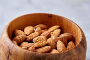 Bowl of almonds on white textured background, top view, close-up, selective focus.