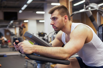 Fototapeta na wymiar Fitness man on bicycle doing spinning at gym. Fit young man working out on gym bike.