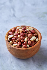 Raw mixed peanuts in wooden plate isolated over white textured background, top view, close-up.