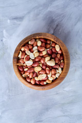 Raw mixed peanuts in wooden plate isolated over white textured background, top view, close-up.