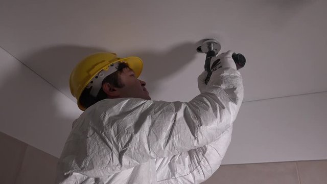 Skilled worker with helmet drilling holes in ceiling