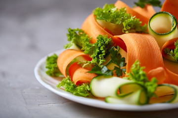 Artistically served vegetable salad with carrot, cucumber, letucce over white background, selective focus