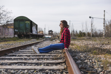 Naklejka premium young beautiful woman wearing casual clothes, sitting on the railway and smiling. Outdoors lifestyle. Travel concept.