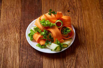 Artistically served vegetable salad with carrot, cucumber, letucce over wooden background, selective focus