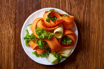 Artistically served vegetable salad with carrot, cucumber, letucce over wooden background, selective focus