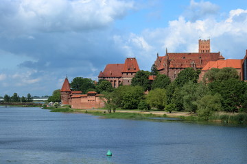 Zamek krzyżacki w Malborku, Polska, widok z przeciwnego brzegu rzeki, na niebie malownicze obłoki - obrazy, fototapety, plakaty