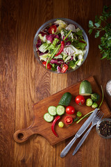 Fresh vegetable salad and ripe veggies on cutting board over wooden background, close up, selective focus