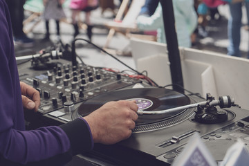 Dj mixing vynil records on open hair - view from the back - focus on the right hand, filtered image