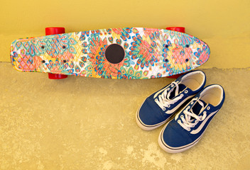 Close up of colorful skateboard next to the wall with sport shoes, extreme sport challenge and skateboarder training urban © olgaminaieva