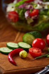 Fresh vegetable salad and ripe veggies on cutting board over wooden background, close up, selective focus