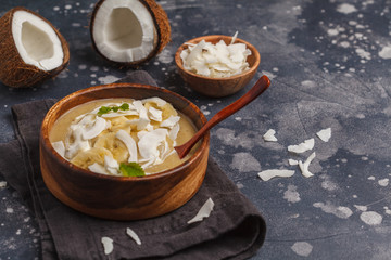 Coconut banana smoothie bowl in a wooden plate on a dark background, vegan healthy food concept. Top view, copy space.
