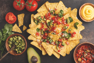 Mexican food concept. Nachos - yellow corn totopos chips with various sauces in wooden bowls: guacamole, cheese sauce, pico del gallo, top view