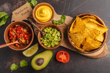 Mexican food concept. Nachos - yellow corn totopos chips with various sauces in wooden bowls: guacamole, cheese sauce, pico del gallo. Top view, food background