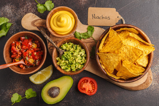 Mexican food concept. Nachos - yellow corn totopos chips with various sauces in wooden bowls: guacamole, cheese sauce, pico del gallo. Top view, food background