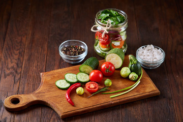 Delicious vegetable salad in jar and fresh veggies on cutting board on table, selective focus, close-up