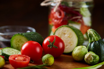 Delicious vegetable salad in jar and fresh veggies on cutting board on table, selective focus, close-up