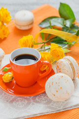 Orange cup of black coffee, yellow roses flowers and sweet pastel french macaroons