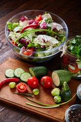 Delicious vegetable salad in jar and fresh veggies on cutting board on table, selective focus, close-up