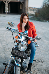 Fototapeta na wymiar beautiful young blue-eyed woman smiling sitting on her motorbike, wearing a jacket and red lips