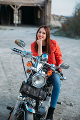 Fototapeta na wymiar beautiful young blue-eyed woman smiling sitting on her motorbike, wearing a jacket and red lips