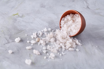 Large white sea salt in a natural wooden bowl on white background, top view, close-up, selective focus