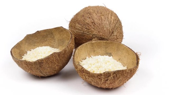 One whole and two shells halves of tropical coconut with dried white coconut flakes rotating on white isolated background. Healthy tropical fruits. Loopable seamless cocos rotating