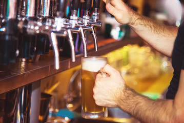 Barman hand at beer tap pouring a draught lager beer serving in a restaurant or pub. Vintage soft effect on photo