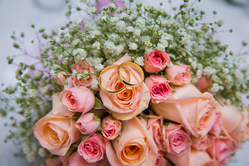 Bridal bouquet with orange and pink roses of different size with handle on white background. Romantic wedding bouquet with beautiful flowers. Two rings represent the meaning of feeling love