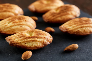 Freshly baked almond cookies with almond on stone board over wooden background, top view, selective focus.