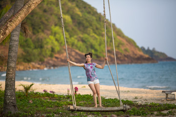 Young mixed race woman on the wooden swings on sea beach.