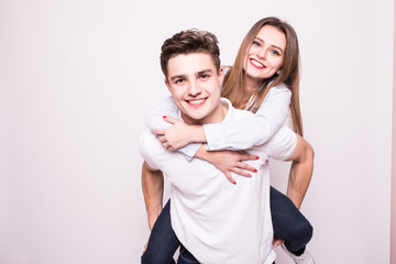 Happy casual man giving pretty girlfriend piggy back on white