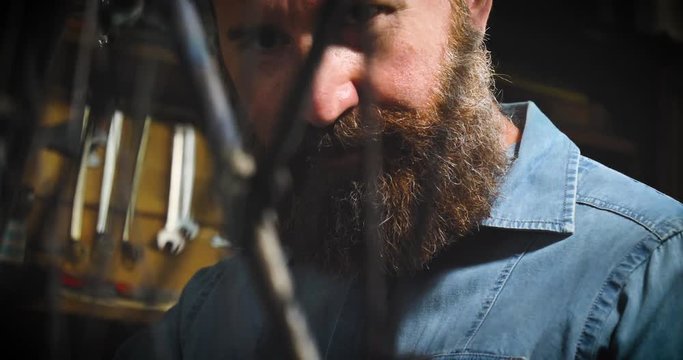 Well-groomed handsome bearded master hipster, specialist in bicycles, repairing a bicycle in his workshop, wheels, frame, spokes, the background of tools. Concept: pro bike, cycle passion, lifestyle.