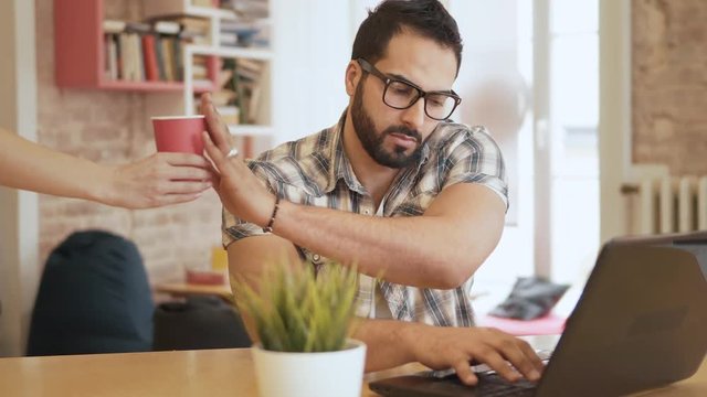 Good-looking busy man refusing to have coffee while working at the computer, successful businessman in stylish glasses typing quickly on black device, sitting in cosy rich office