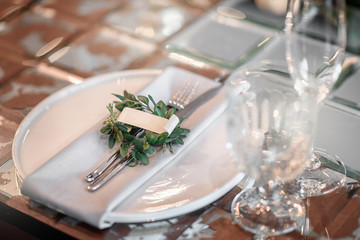 Mirror table served with plates, forks, spoons, glasses,  napkins in the restaurant. Beautiful festive table decorated with fresh flowers