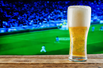 Glass of beer on a football game TV background