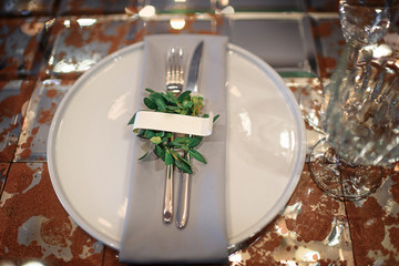 Mirror table served with plates, forks, spoons, glasses,  napkins in the restaurant. Beautiful festive table. White dish on the background of a mirror table, top view
