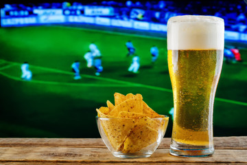 Glass of beer and snack on a football game TV background