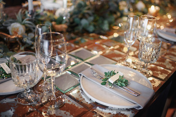 Mirror table served with plates, forks, spoons, glasses,  napkins in the restaurant. Beautiful festive table decorated with fresh flowers and candles