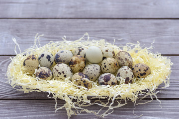Quail eggs in straw on wooden background