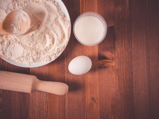 Plate with flour, eggs and a wooden rolling pin on a wooden background. Top view
