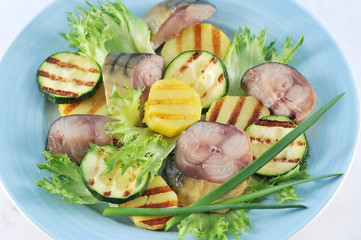 Slices of smoked mackerel and vegetables cooked on the grill (potatoes and zucchini). The appetizer is decorated with green onions and lettuce leaves. View from above. Close-up. Macro photography.