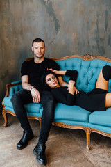 Young beautiful couple in dark clothes on a turquoise vintage couch.